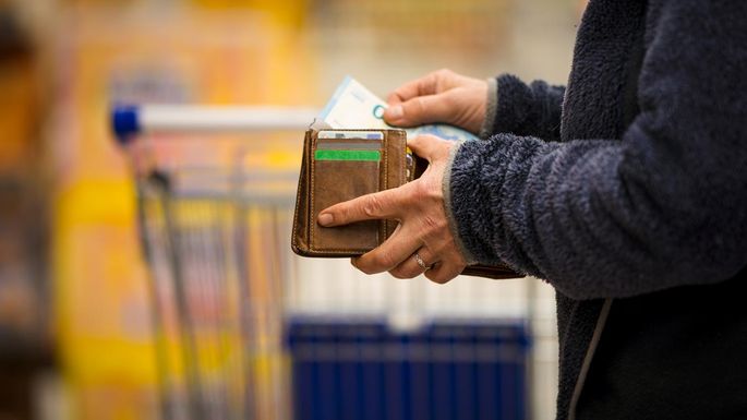Eine Person steht mit einem Portemonnaie in der Hand im Supermarkt und zieht einen 20-Euro-Schein heraus